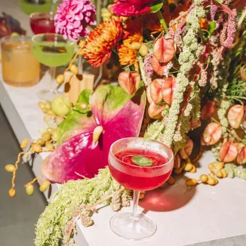Cocktail glass surrounded by a vibrant variety of flowers and plants.