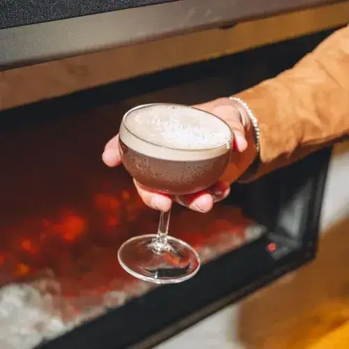 A hand holding a cocktail glass with a fizzy drink.