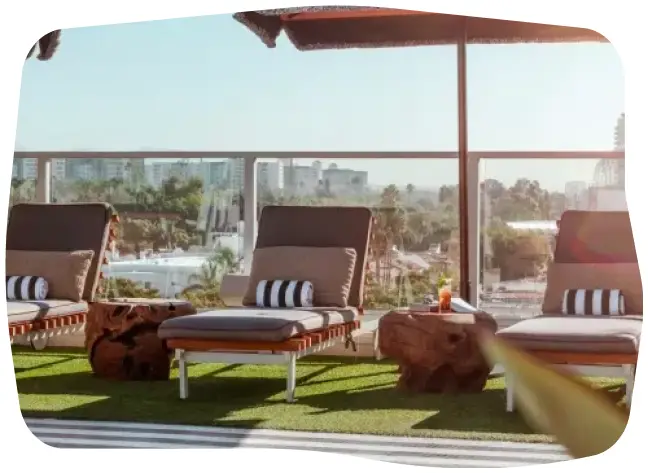 Outdoor terrace with two loungers, a tree trunk table, and a panoramic view of the city in the background.